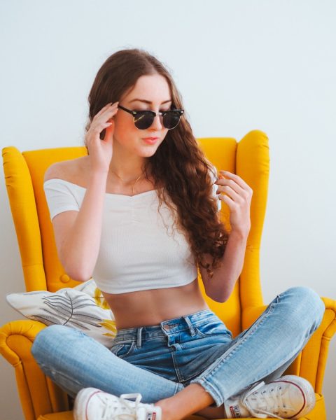 woman in white tank top and blue denim jeans wearing black sunglasses sitting on yellow leather