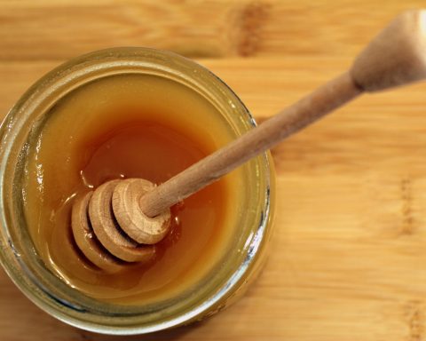 Een glazen pot honing met een houten lepel op een houten ondergrond