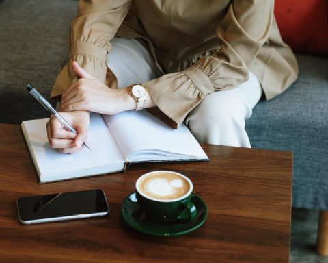 Jonge vrouw schrijft in een notitieboekje met een kop koffie naast zich, bezig met zelfreflectie