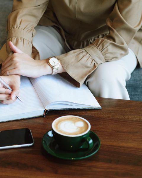 Jonge vrouw schrijft in een notitieboekje met een kop koffie naast zich, bezig met zelfreflectie