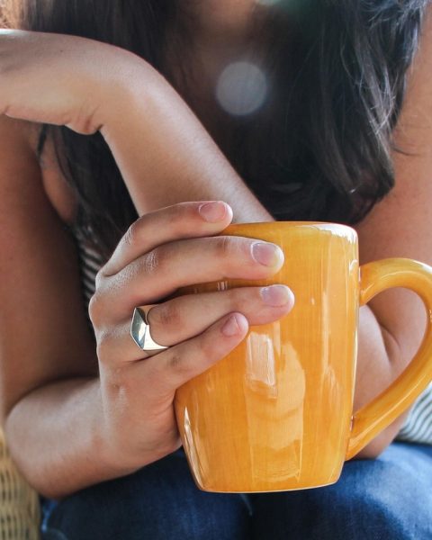 Jonge vrouw schrijft in een notitieboekje aan de keukentafel met een kop koffie naast zich